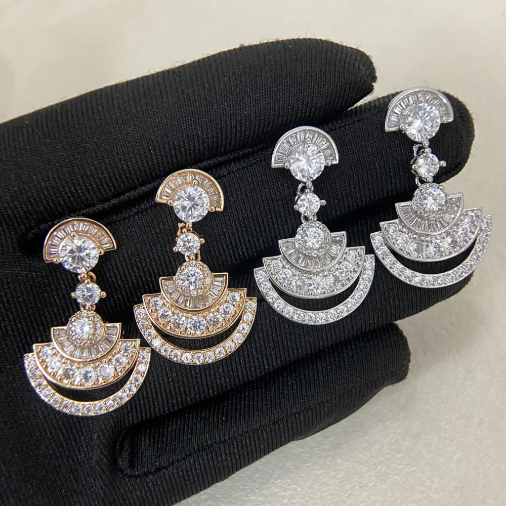 Two pairs of fan-shaped earrings, rose gold and silver, resting on a black glove